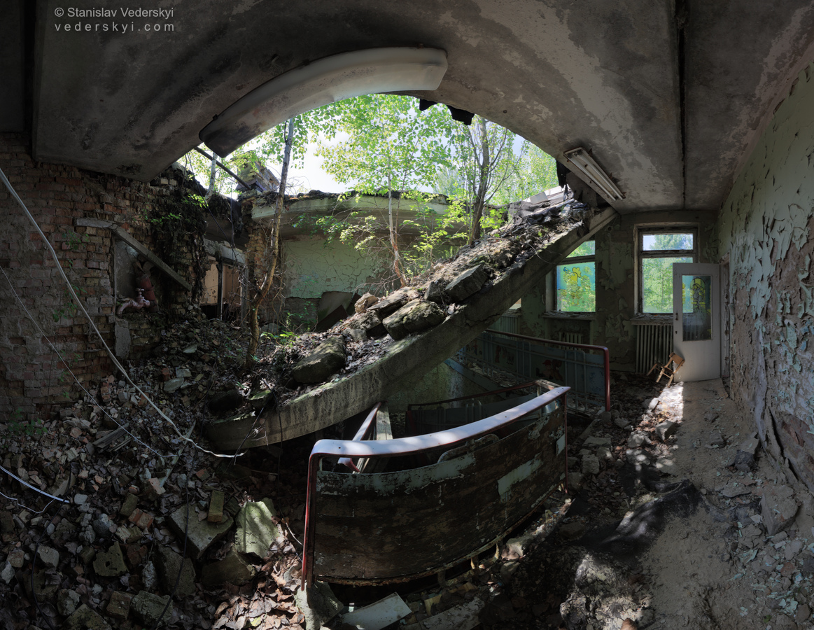 Pripyat-Ruined Kindergarten-1-1100×900 Chernobyl zone Multirow panorama of abandoned ruined kindergarten staircase with collapsed concrete slab of roof covered with trees and bushes lit by bright sunshine in derelict Pripyat ghost town of Chernobyl zone of alienation.